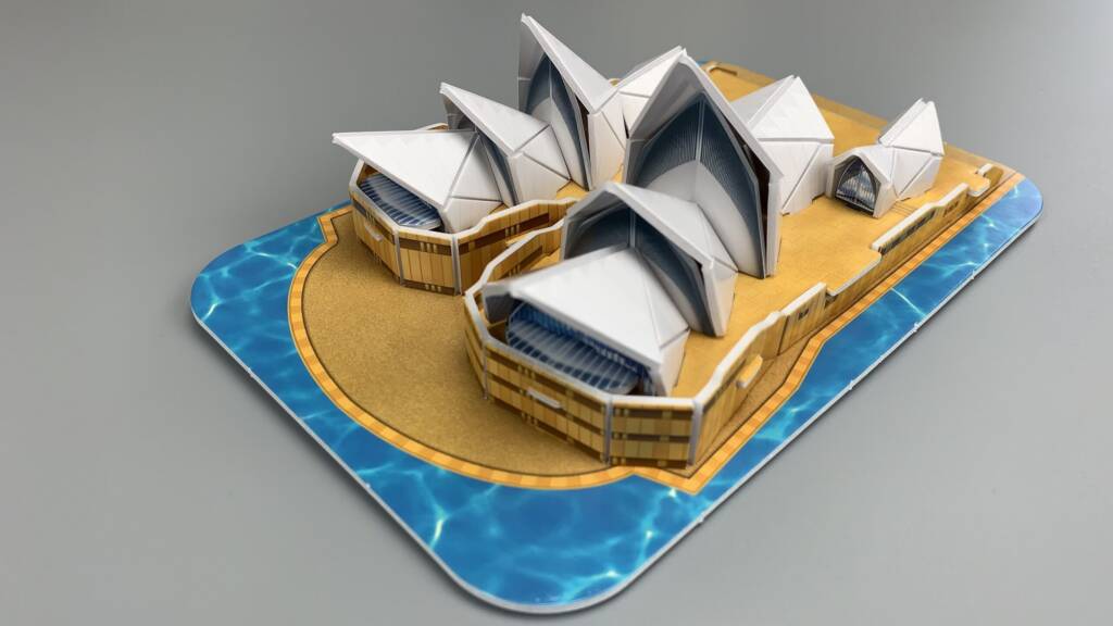 Sydney Opera House model with white sail-like roofs and blue harbour pool base, angled view.