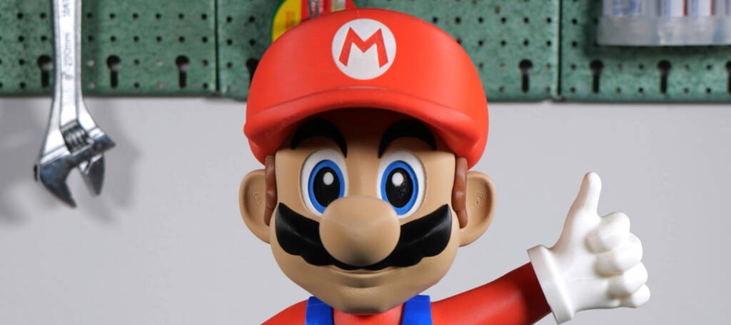 Super Mario with red cap and “M” logo, mustache and blue overalls giving a thumbs-up