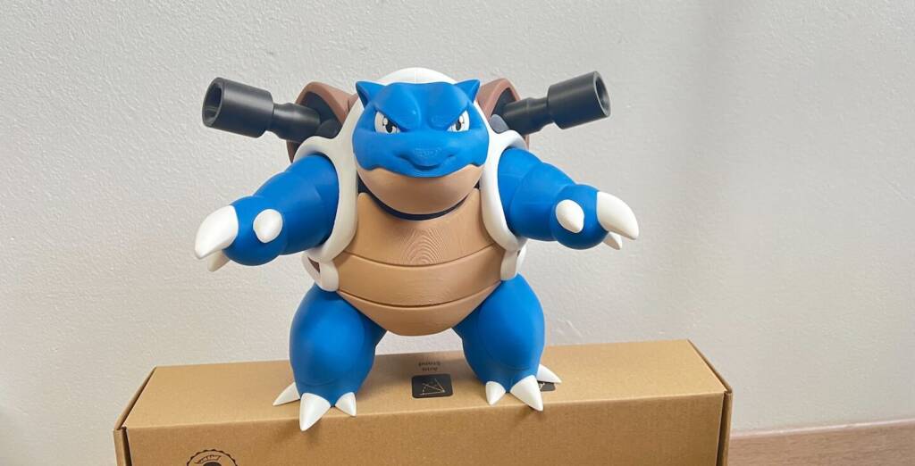 Blue blue-and-white creature wearing goggles, holding black bazookas, standing on a shipping box