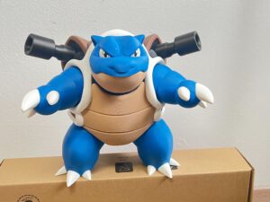 Blue blue-and-white creature wearing goggles, holding black bazookas, standing on a shipping box