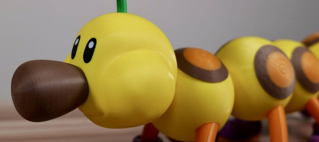 Yellow cartoon wiggler toy with brown beak and orange feet, close-up on a tabletop