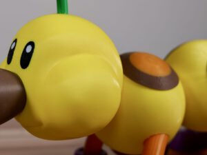 Yellow cartoon wiggler toy with brown beak and orange feet, close-up on a tabletop