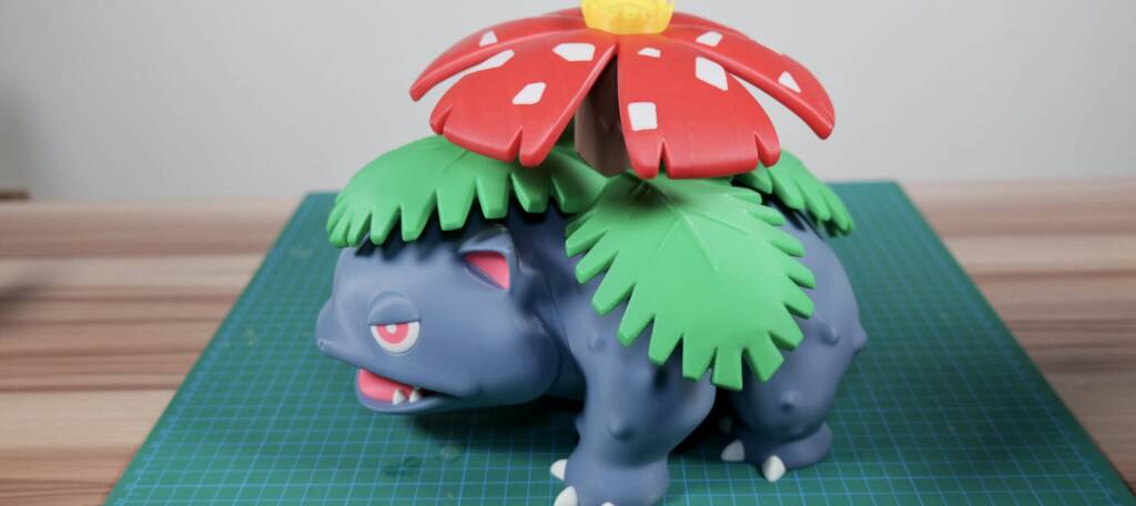 Venusaur figurine with red flower canopy and green vine-like frills on a cutting mat