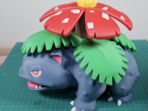 Venusaur figurine with red flower canopy and green vine-like frills on a cutting mat