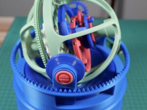 3D printed robotic gear mechanism with blue ring gears and red center, on green cutting mat