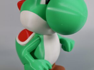 3D-printed Yoshi figurine with green shell and brown shoes posed mid-step against a gray background