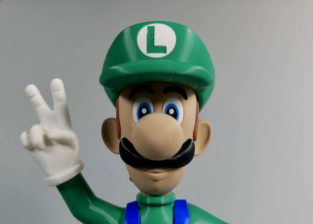 Luigi in green hat and blue overalls making a peace sign with his gloved hand