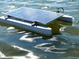 Solar panels mounted on a floating catamaran hull on calm water, with cabling and connectors visible