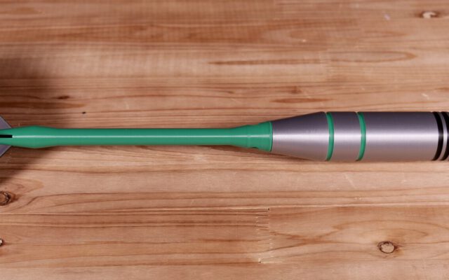 Giant dart with green shaft and silver barrel on a wooden floor, tip pointing right