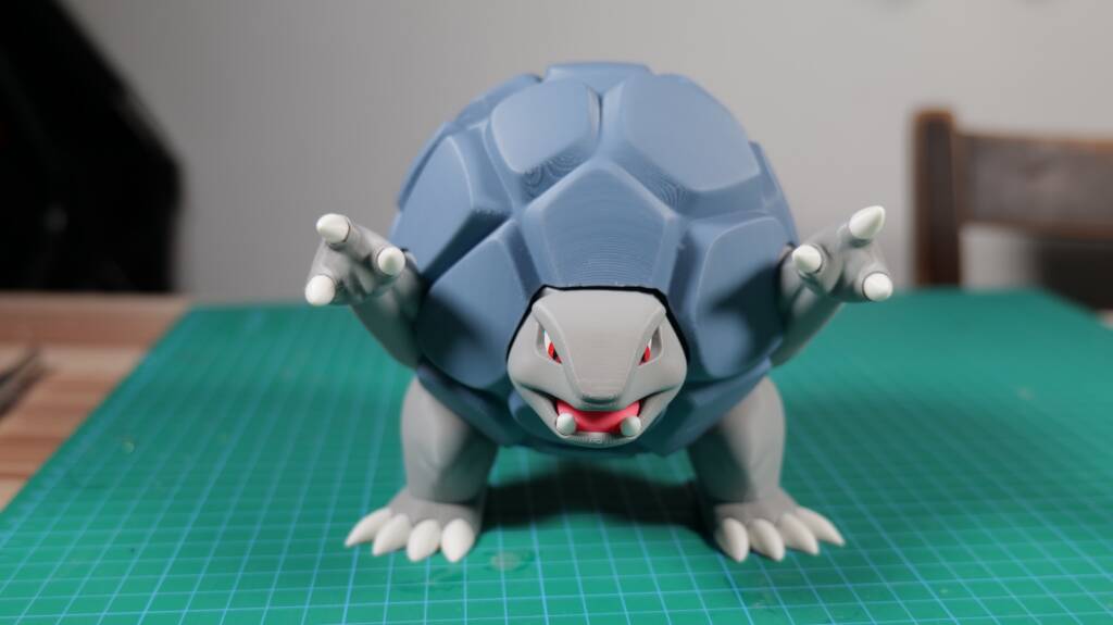Blue mechanical dragon figurine with red eyes crouched on a green cutting mat for model building