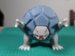 Blue mechanical dragon figurine with red eyes crouched on a green cutting mat for model building